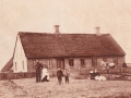 Gårdmand og købmand i Vind Kirkeby, Jens Christian Jensen (1867-1938) og hustru Ane Kathrine Jensen (f. Thomsen, 1869-1947) samt deres tre ældste sønner fotograferet omkring 1899 foran ejendommen, der senere har fået navnet Toftegård, i dag Præstevejen 35. Midt i billedet -hånd i hånd- ses Niels Peter Jensen (1893-1970) og Mogens Kristian Jensen (1895-1969). Længere til højre, sammen med hvad der formodes at være en stue- eller tjenestepige, Karl Marius Jensen (1897-1988). Personen yderst til højre har ikke kunnet identificeres.