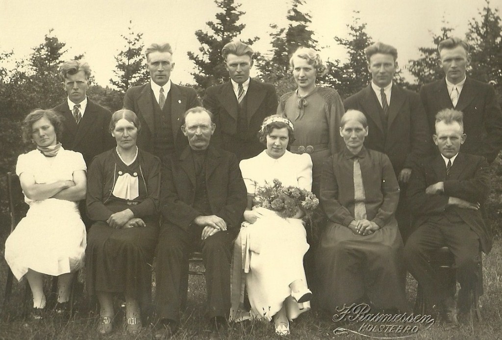 Familien Jensen fra Mikkelborg samlet til familiebryllup i 1937. Siddende fra venstre ses Ane Johanne Jensen (g. Nielsen, 1901-1955), Kristine Jensen (g. Rasmussen, 1894-1979), Jens 'Mikkelborg' Jensen (1868-1942), Dagmar Jensen (g. Hansen, 1907-1983), Laura Margrethe Jensen (f. Andersen, 1870-1947) og Peder Jensen (1896-1987). Stående fra venstre ses Jens Kristian Jensen (1904-1971), Karl Jensen (1899-1961), Valdemar Jensen (1909-1991), Alma Jensen (g. Jeppesen, 1914-2004), August Jensen (1905-1993) og Gunnar Jensen (1911-1946).